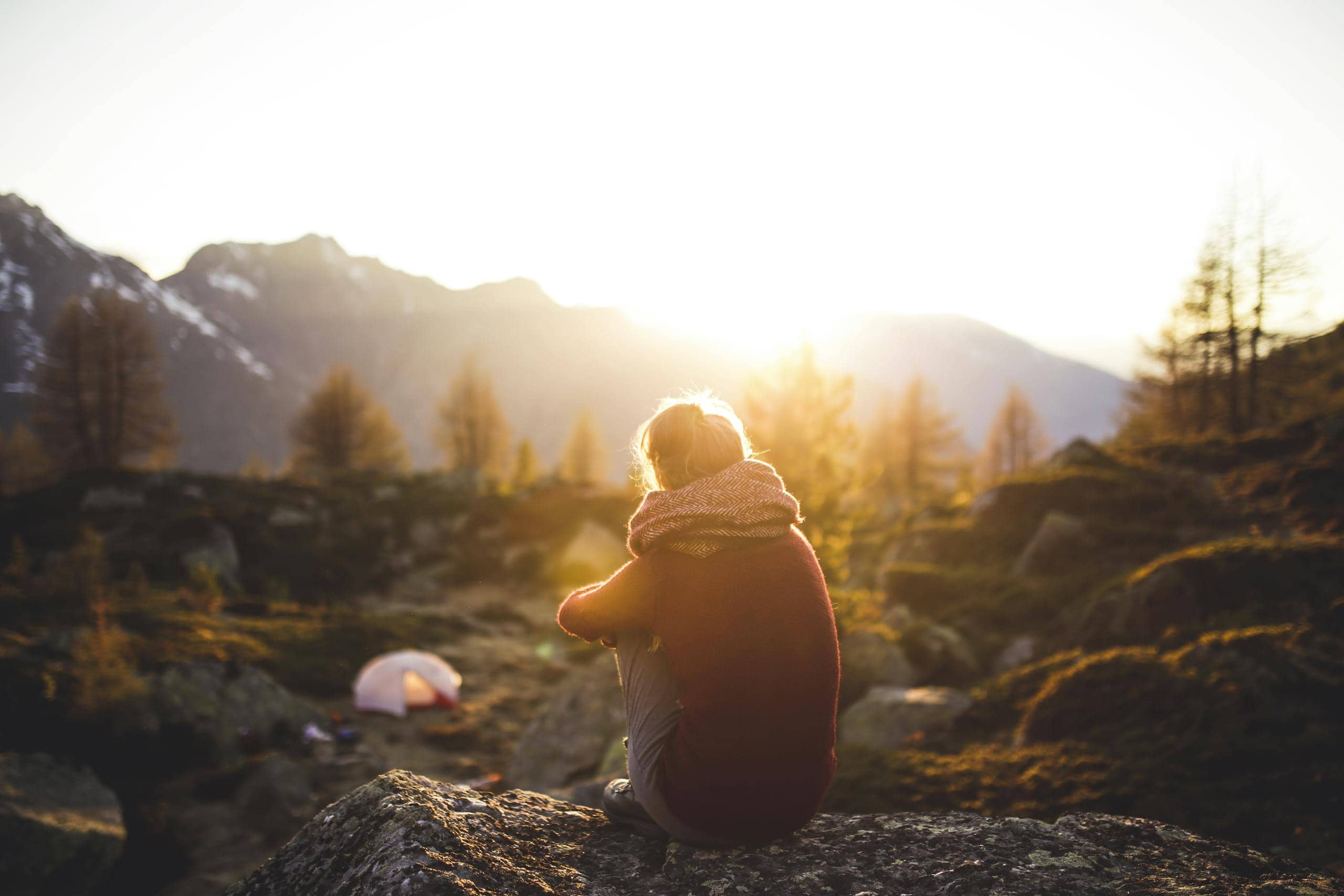 A woman sits on a rock enjoying the serene mountain view at sunrise in Sachseln, Switzerland.